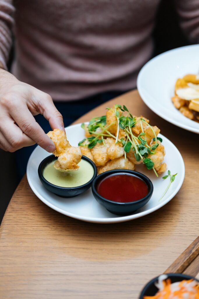 Close-up of a hand dipping crispy tofu bites into sauces, garnished with microgreens.